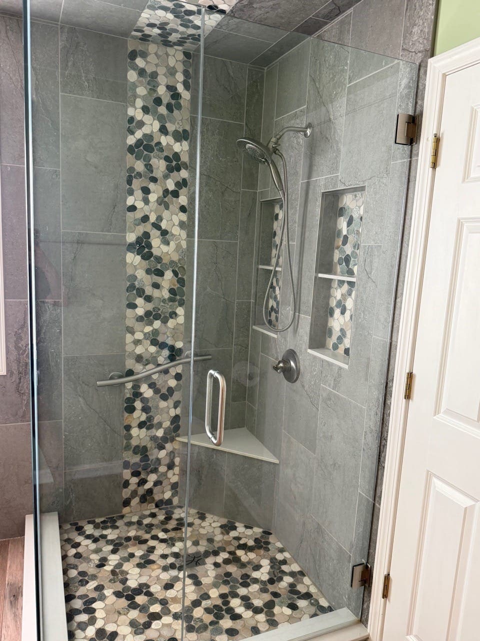 Glass-enclosed shower with a pebble-tile accent strip and a recessed shelf, cleaned