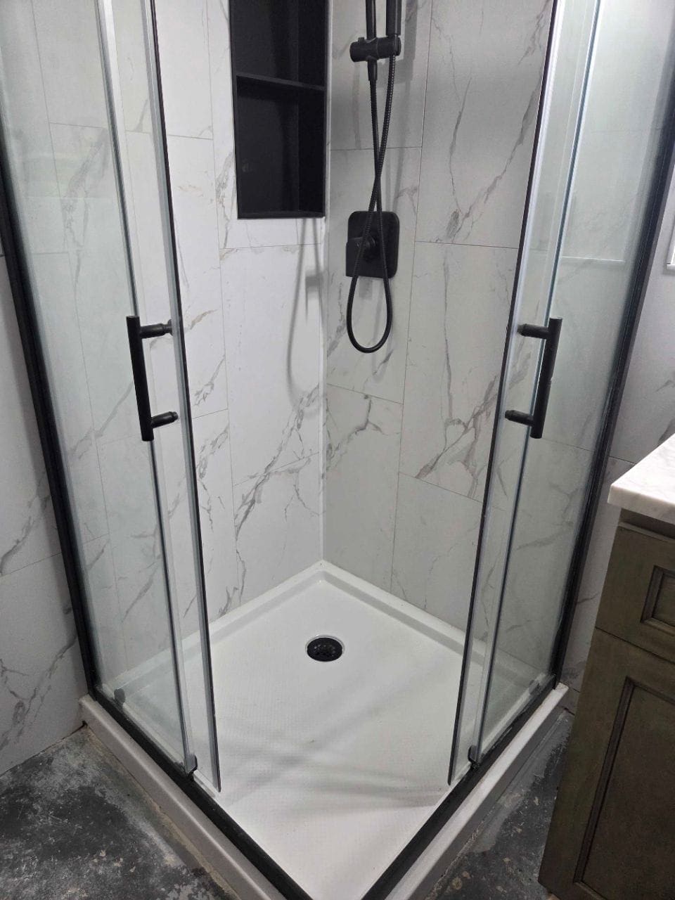 Shower stall with marble-look tile and a black-framed glass door, cleaned