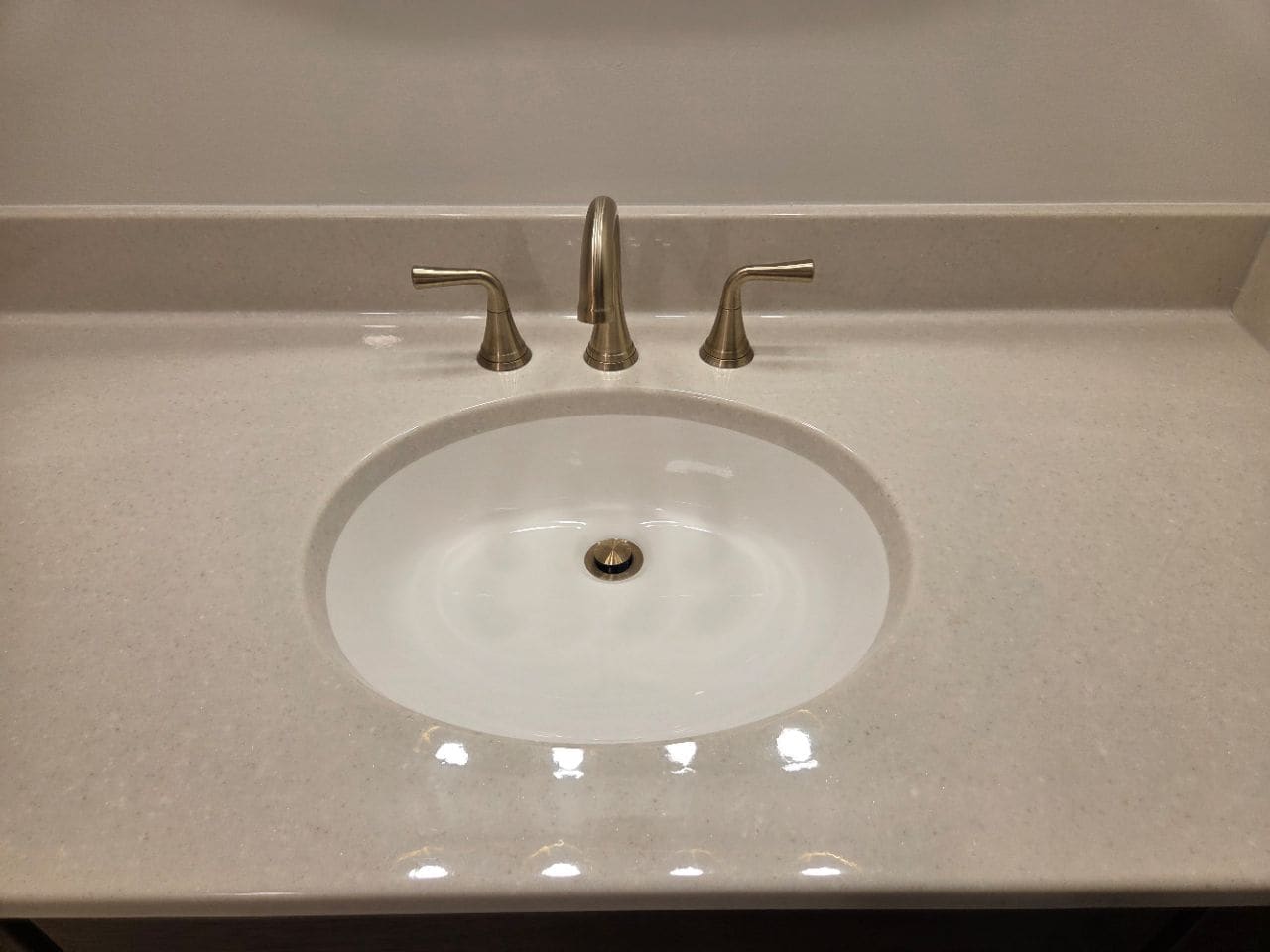 Oval sink with a gold-tone faucet on a cream counter, cleaned
