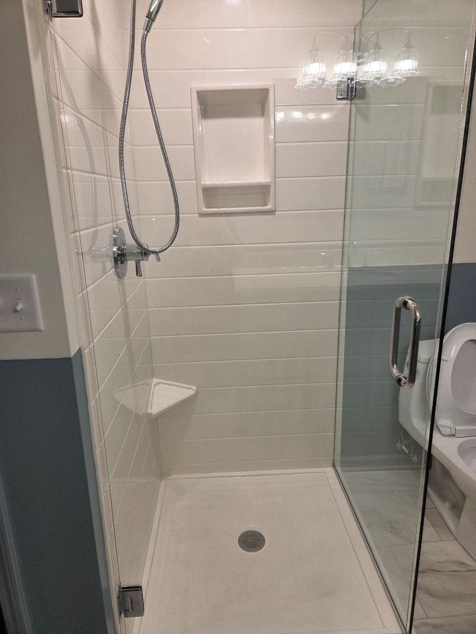 Tiled shower with a glass door and a corner shelf, cleaned