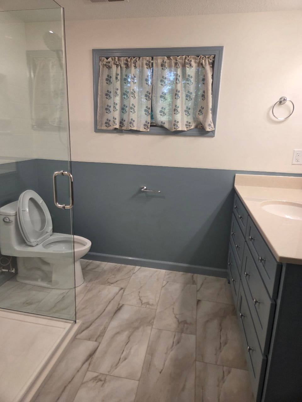 Bathroom with a glass shower door, a gray-blue lower wall, and a toilet, cleaned