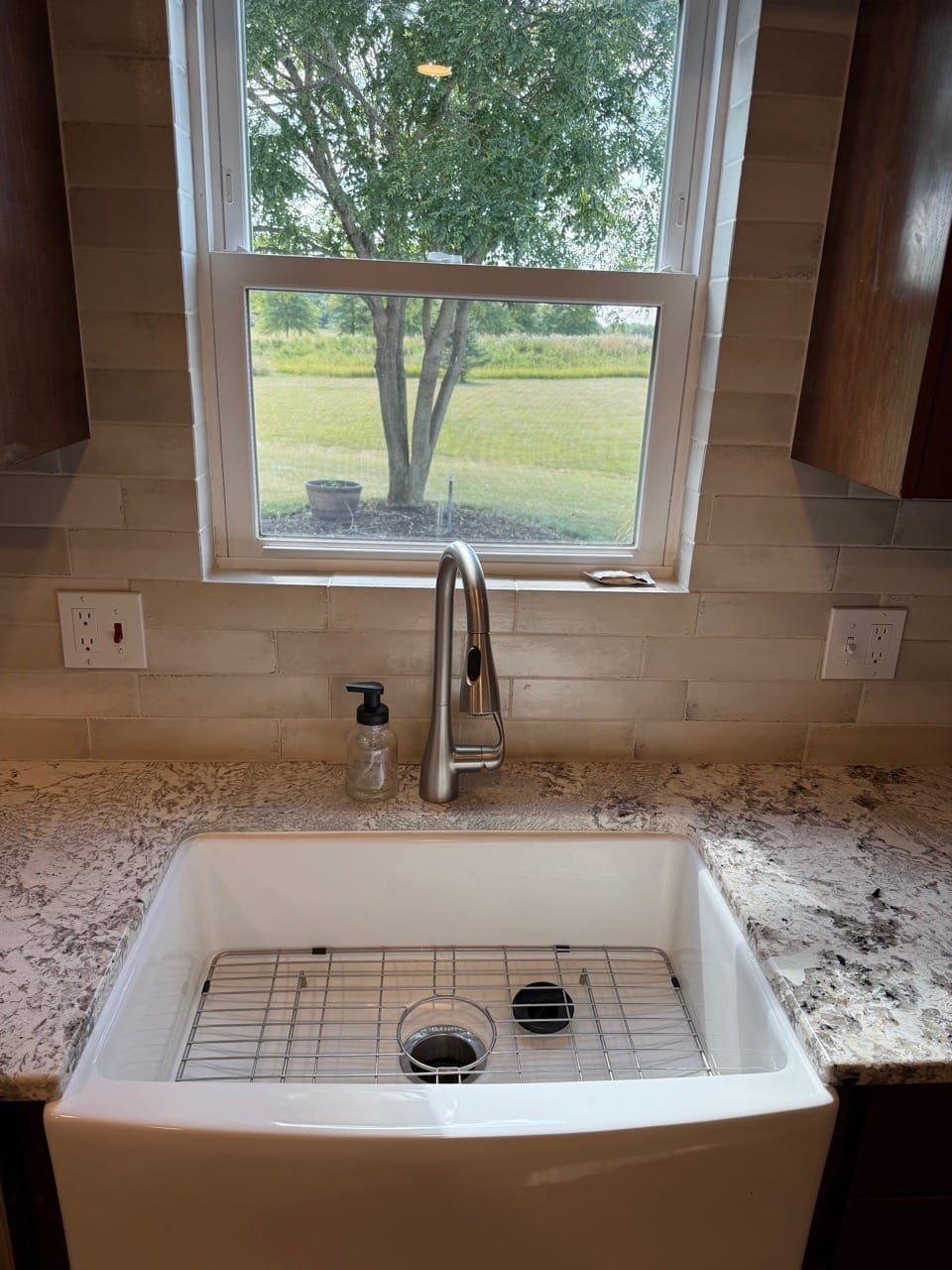 White farmhouse sink under a window with a granite counter, cleaned
