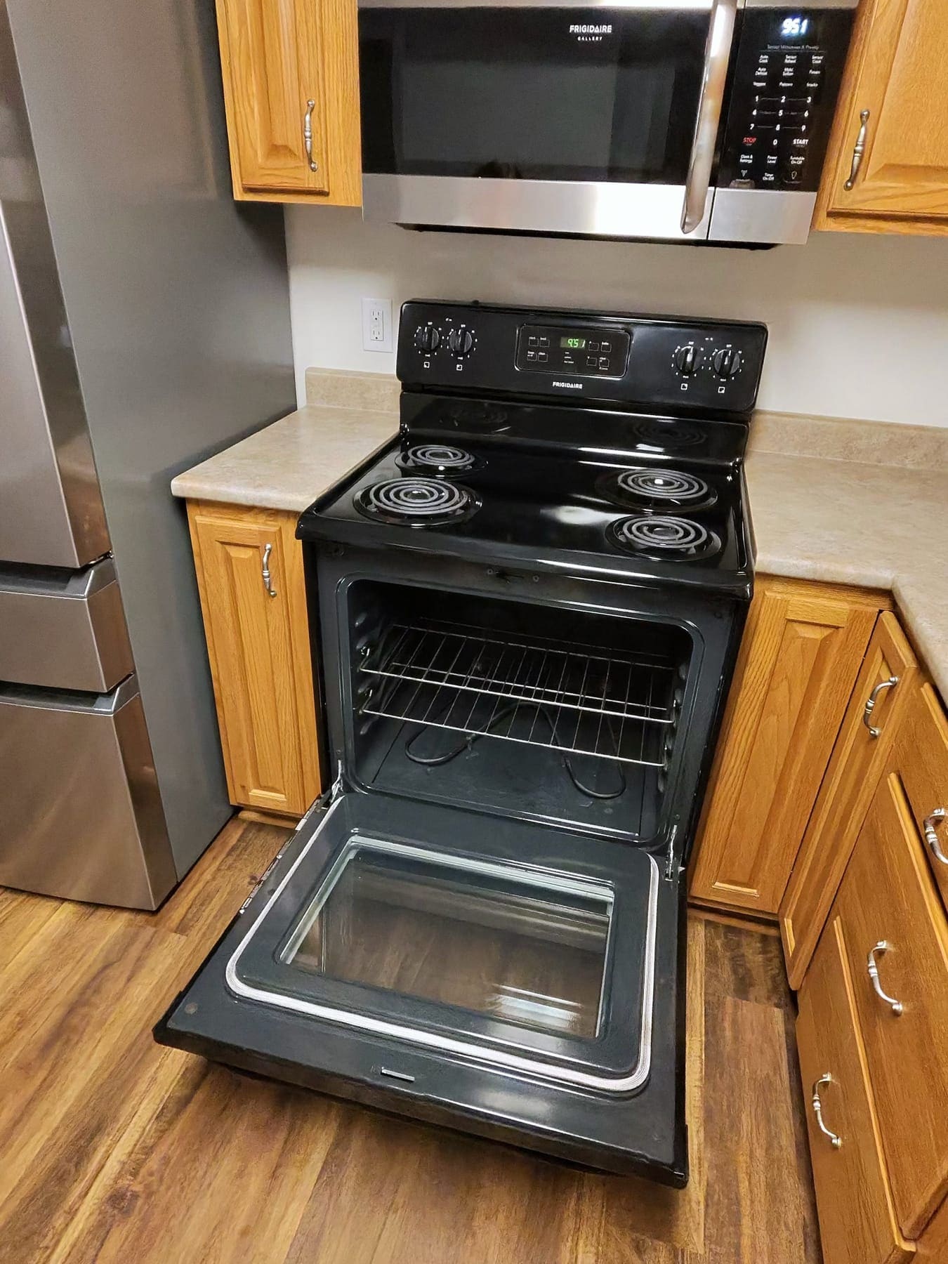 Open electric oven with a clean interior, between wood cabinets