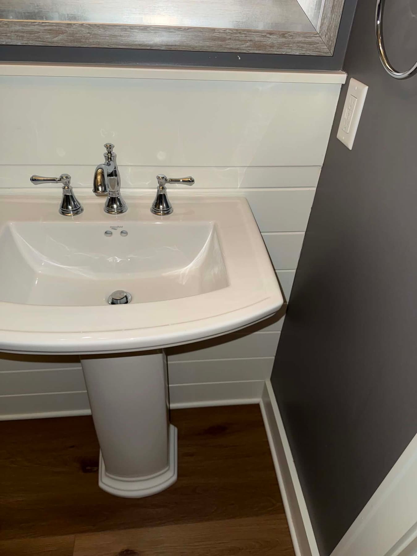 White pedestal sink with chrome faucets against dark walls, cleaned