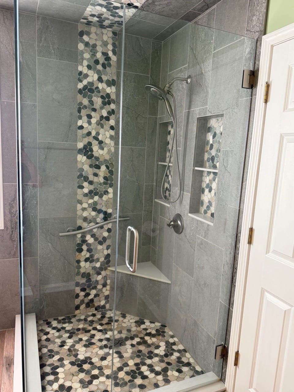 Glass-enclosed shower with a pebble-tile accent strip and a recessed shelf, cleaned