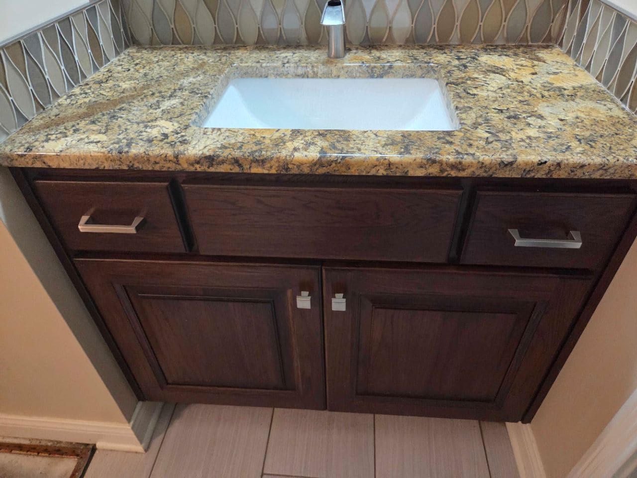 Granite-top vanity with a rectangular white sink and dark wood cabinet, cleaned