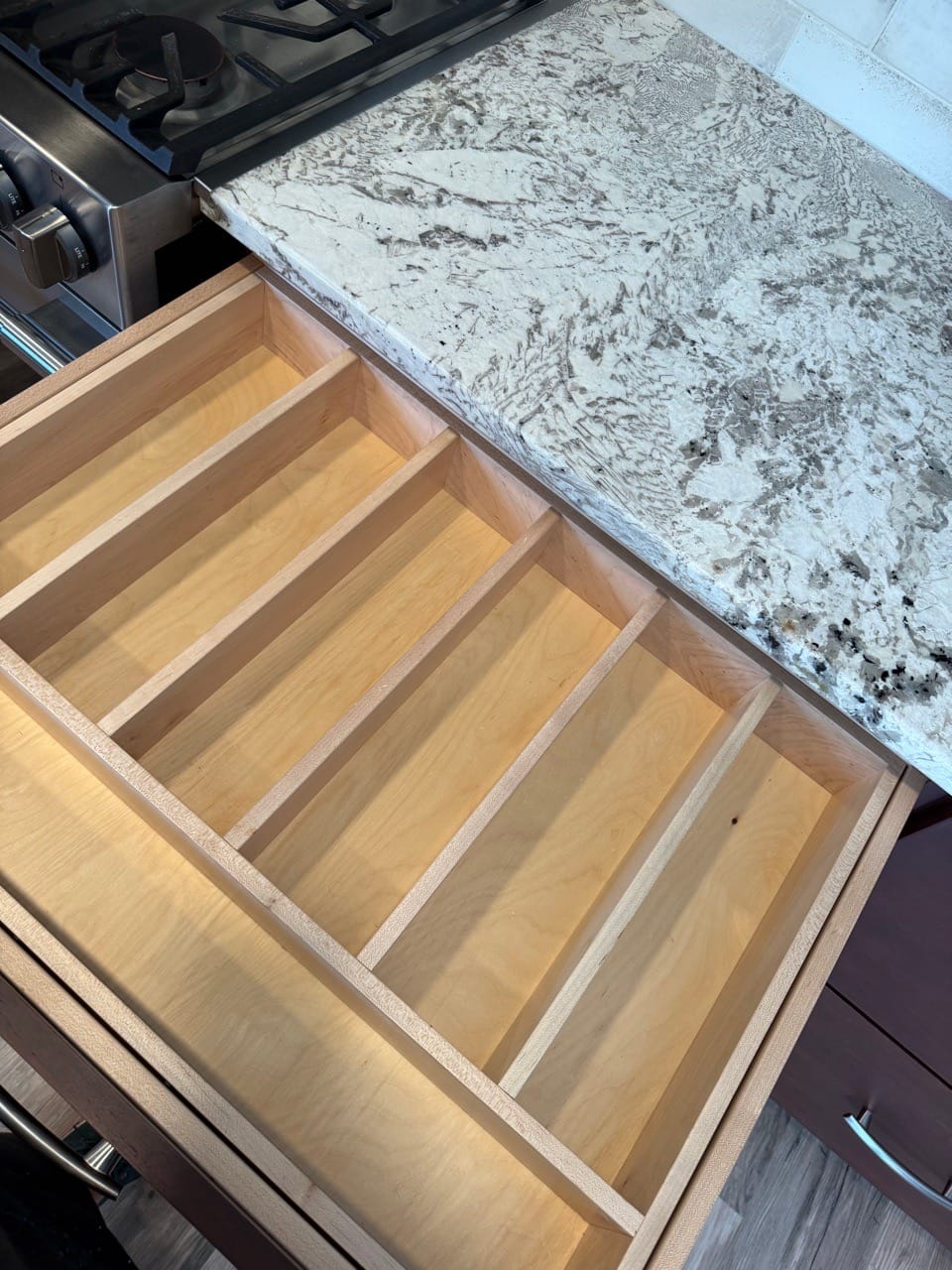 Open kitchen drawers with wood dividers under a granite counter, cleaned