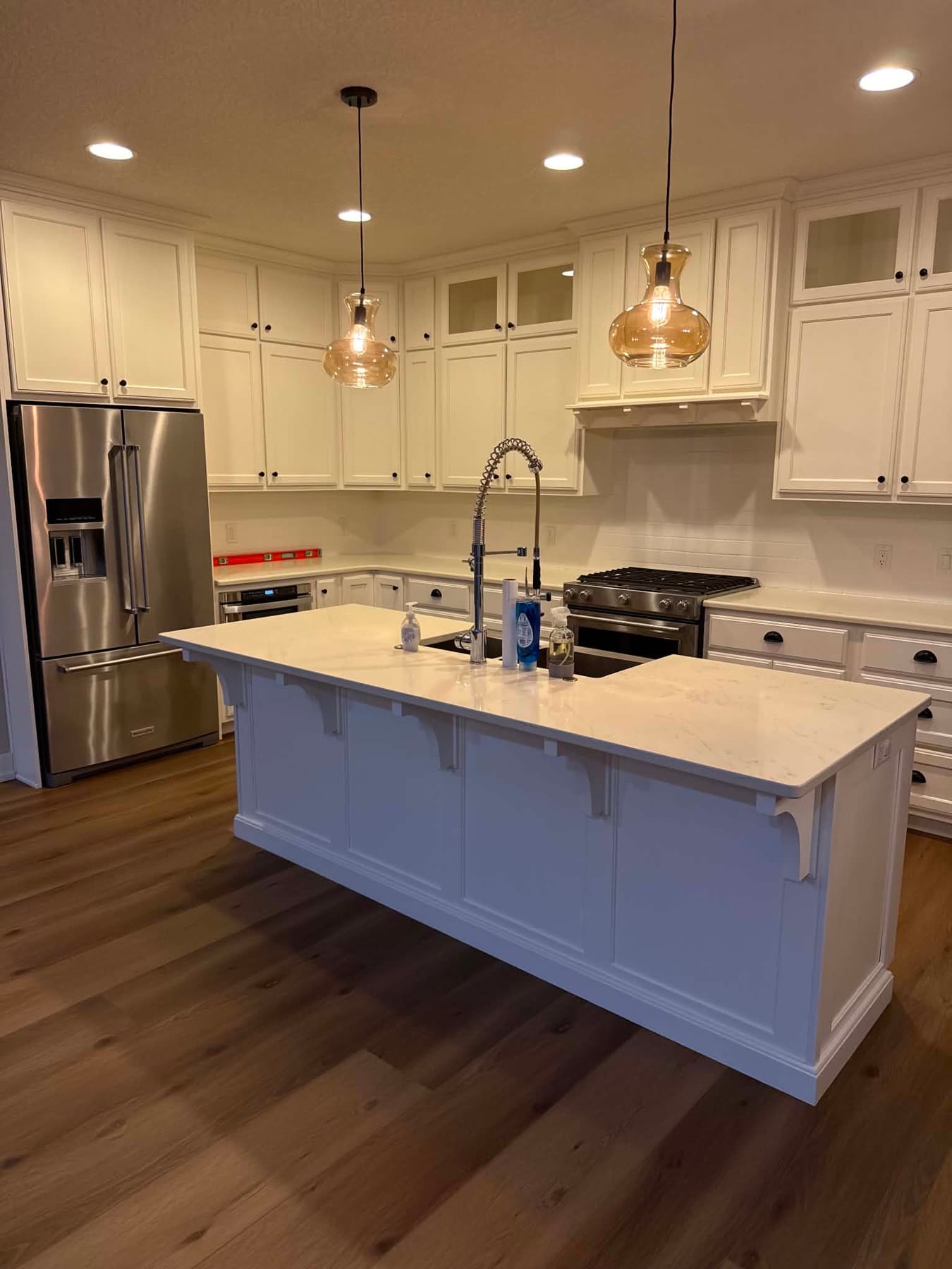 White kitchen island with a sink, pendant lights, stainless appliances, and a wood-look floor, wiped clean